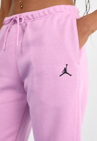 Pantalons de jogger en coton rose avec une taille élastique à cordon et des poches latérales, arborant un logo Jumpman noir sur la cuisse gauche.