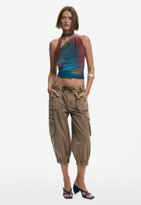 Top halter multicolor cu un gradient de la roșu la albastru, asortat cu pantaloni cargo khaki cu buzunare laterale și manșete elastice, purtați cu tocuri albastre.