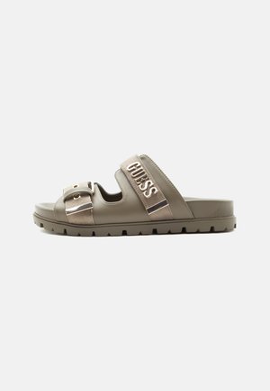 Sandale beige à enfiler avec deux brides réglables, l'une avec une boucle et l'autre embossée du mot "GUESS", avec une semelle épaisse et rainurée.