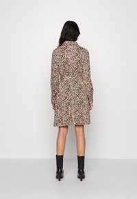 Långärmad klänning i beige med svarta tigerstrimmor, har en insvängd midja och når strax ovanför knäet, kombinerad med svarta ankelboots.