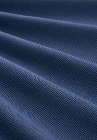 Texturiertes Gewebe in tiefblauer Farbe, das ein Rautenmuster mit gewellten Falten aufweist und seine gewebte Struktur sowie die weiche Textur zur Schau stellt.