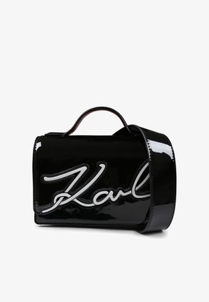 Sac à main en cuir verni noir avec un logo "Karl" blanc bien en évidence, forme structurée, anses supérieures et bandoulière amovible.
