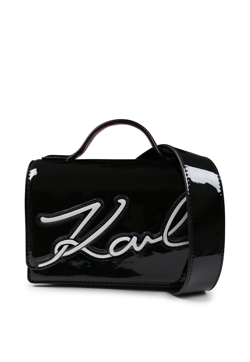 Sac à main en cuir verni noir avec un logo "Karl" blanc bien en évidence, forme structurée, anses supérieures et bandoulière amovible.