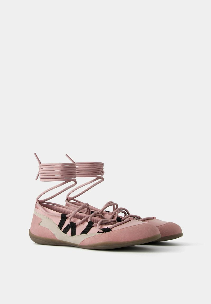 Zapatos planos rosa con un diseño flexible. Cuentan con correas cruzadas y un acento negro en contraste. Parte superior texturizada con punta redondeada.