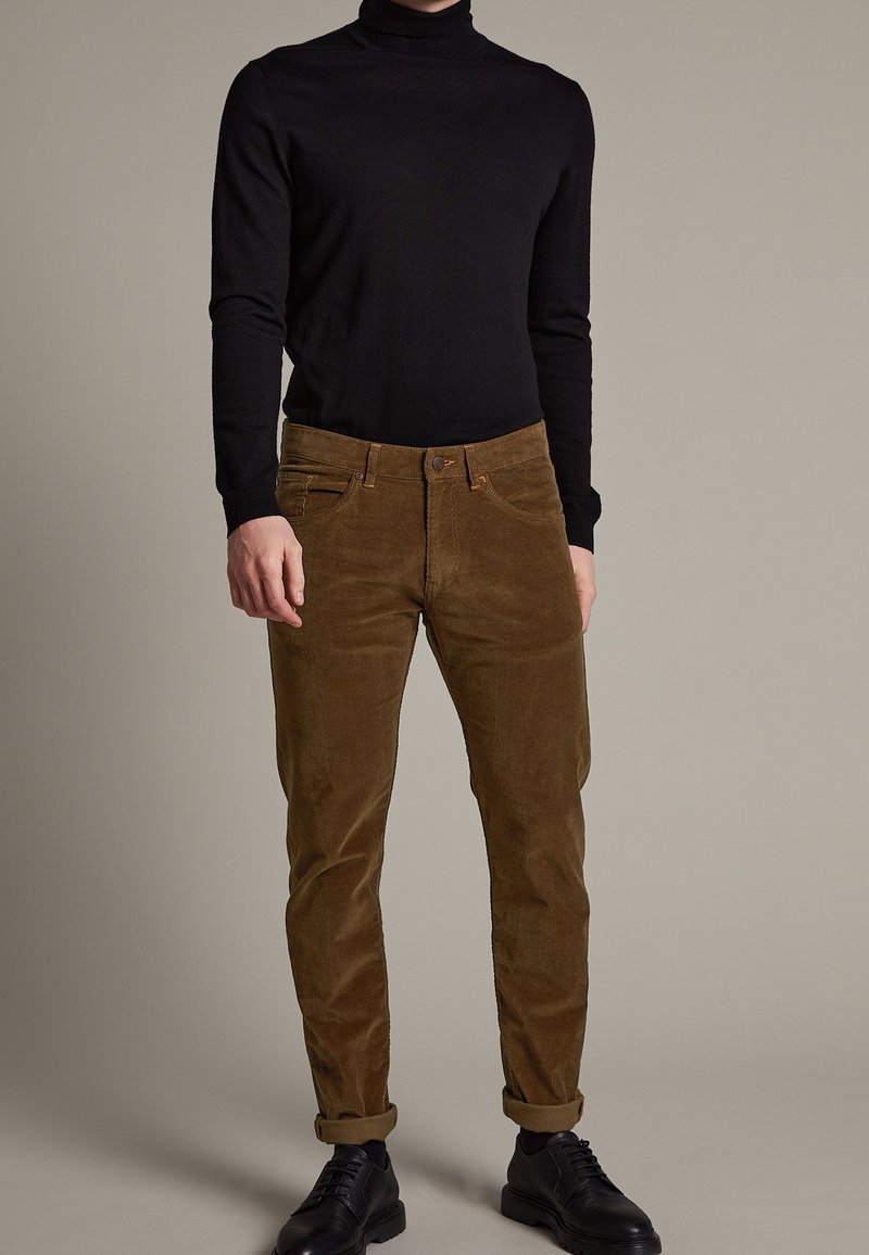 Black turtleneck sweater paired with brown corduroy pants. Pants feature a straight cut and rolled cuffs. Black shoes complete the outfit.