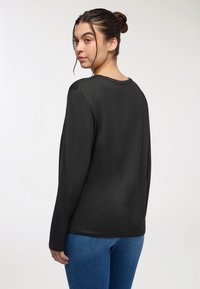 Maglietta nera a maniche lunghe con scollatura rotonda e texture liscia, abbinata a jeans denim blu, vista da dietro.