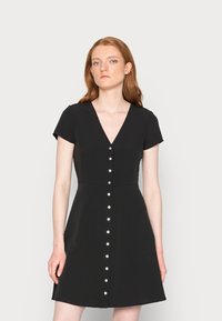 Vestido curto preto de mangas curtas com decote em V e silhueta em A. Apresenta uma linha de botões prateados na parte frontal. Tecido suave com uma textura macia.