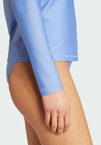 Light blue long-sleeve swim top made of smooth fabric, featuring a round neckline and fitted design, paired with a low-rise bikini bottom.