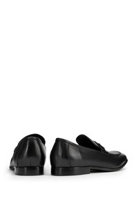 Mocasines de cuero negro con una textura suave, perfil bajo y punta redondeada. Cuentan con costuras sutiles y un leve tacón.