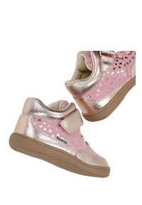 Chaussures roses pour enfants avec des accents métalliques dorés, motifs en forme de cœur, bride velcro et semelles en caoutchouc marron flottant sur un fond blanc.