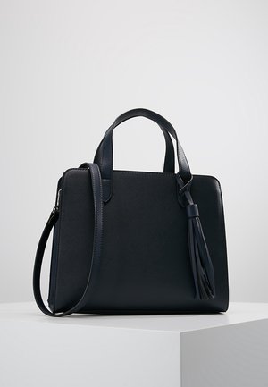 Czarna skórzana torba na ramię z dwoma uchwytami, długim paskiem na ramię i dekoracyjnym chwostem, umieszczona na białej powierzchni na tle szarego tła.