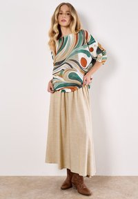 Camicia multicolore con motivi astratti, abbinata a una lunga gonna beige. Stivaletti marroni completano l'outfit.
