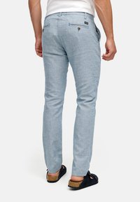 Lichtblauwe linnenbroek met een slanke pasvorm, voorzien van achterzakken met knoopsluitingen en een ceintuurlus in de taille. Soepele textuur.