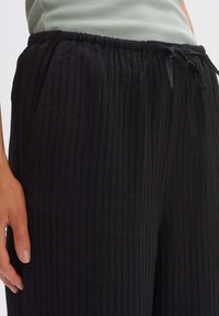 Black pleated pants made of lightweight fabric. Features an elastic waistband, drawstring closure, and side pockets.