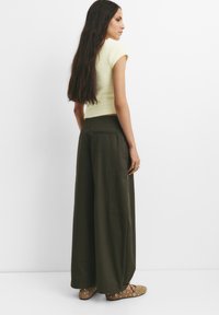 Olijfgroene wijde broek met twee achterzakken, gecombineerd met een lichtgele geribbelde T-shirt met korte mouwen en een paar bruine flats met gaatjesaccenten.