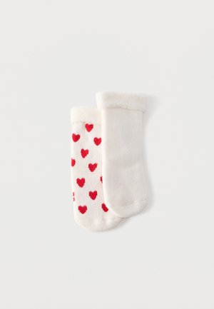 Ζευγάρι από μαλακές λευκές κάλτσες για μωρό, μία μονόχρωμη και μία με κόκκινα καρδιές, και οι δύο με διπλωμένες μανσέτες.