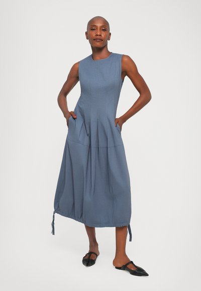 Mėlyna be rankovių suknelė su prigludusia palaidine, klostuotu sijonu, šoninėmis kišenėmis ir surinktu kraštu su raišteliais; lygus paviršius, iki blauzdų ilgio.