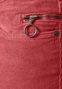 Tissu en velours côtelé rouge avec une tirette de fermeture éclair en anneau métallique et un petit bouton en métal sur une poche.