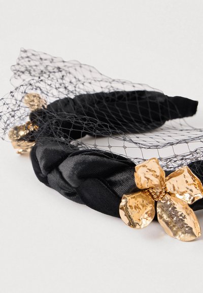 Μαύρη πλεκτή κορδέλα με χρυσό μεταλλικό λουλούδι και λεπτομέρειες από μαύρο δίχτυ. Λείο σατέν υφή με γυαλιστερό φινίρισμα στο λουλούδι.
