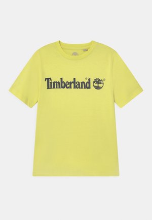 Żółta koszulka z krótkim rękawem i okrągłym dekoltem, z czarnym napisem "Timberland" i logo drzewa umieszczonym centralnie na piersi.