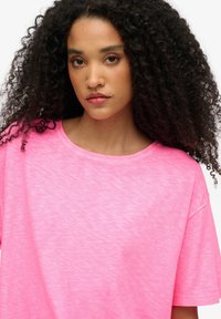 Camiseta de manga corta de color rosa brillante, hecha de tela suave. Presenta un ajuste relajado y un escote redondo; el sutil diseño de jaspeado añade textura.