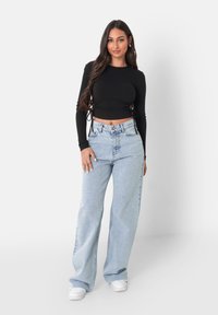 Svart långärmad croppad topp med sidoknytningar, tillsammans med ljusblå högmidjade vida jeans och vita sneakers.