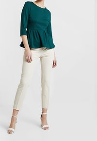 Teal peplumtop met driekwartmouwen, gecombineerd met crèmekleurige slim-fit broek en witte sandalen met bandjes. Glad stof met een gestructureerd ontwerp.