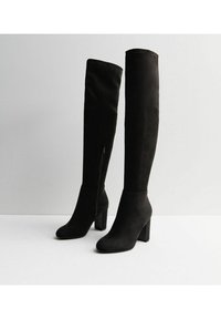 Botas negras de ante sobre la rodilla con tacón cuadrado. Cuentan con una cremallera lateral y una silueta suave y estilizada.