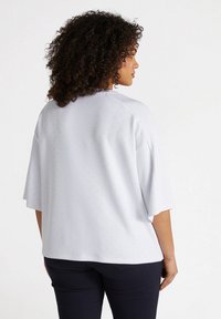White top with a loose fit and short sleeves, featuring small, subtle dot patterns throughout. Smooth texture and soft fabric.