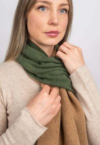Strikket tørklæde med en grøn øverste del og en beige nederste del, begge med en blød tekstur og en afslappet fald på en lys baggrund.