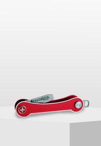Multi-tool rouge au design courbé. Il présente un accent argenté et un emblème croisé proéminent, fabriqué en matériau durable et de taille compacte.