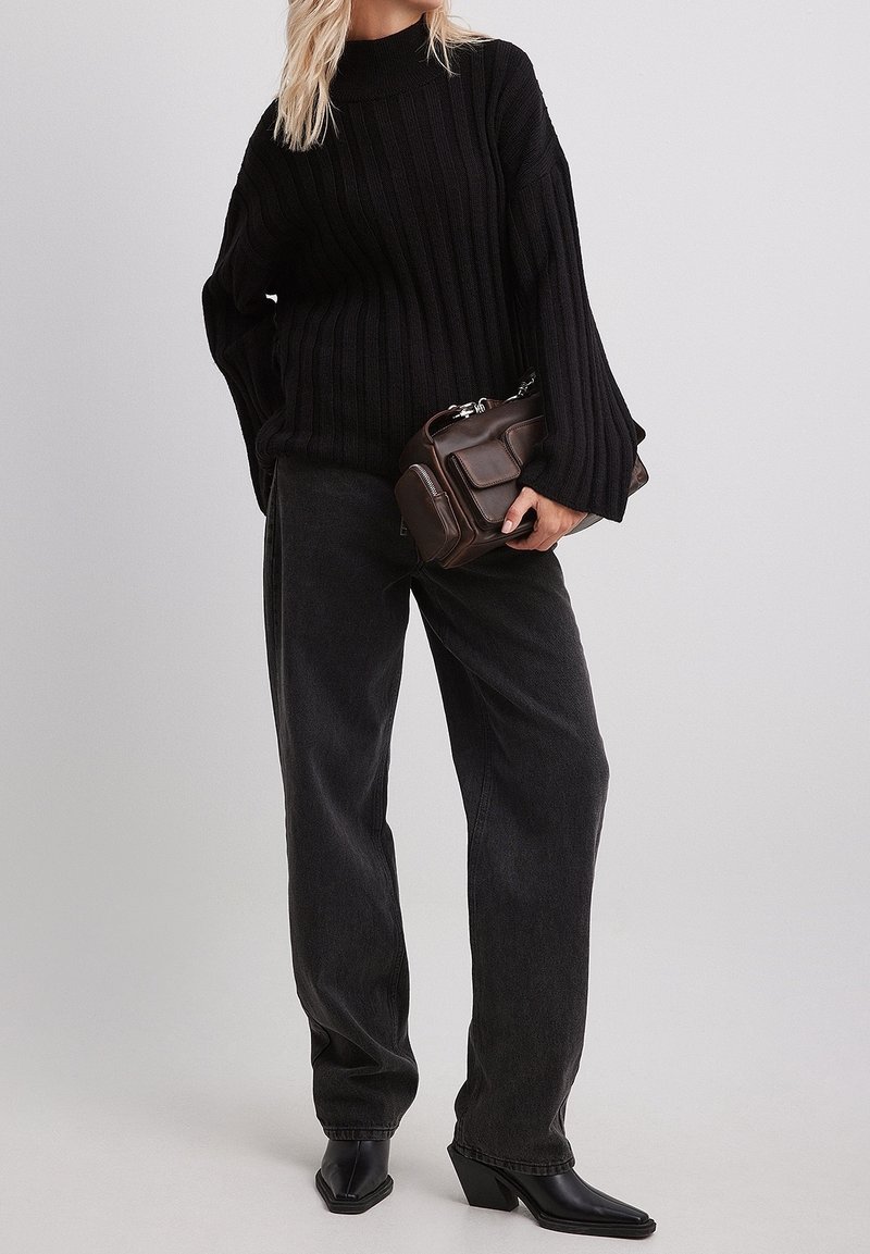Pull noir côtelé avec des manches larges, associé à un jean noir taille haute. Sac à main marron texturé et bottines noires à talons.