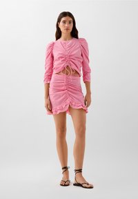 Rød og hvid ternet crop top med pufærmer og snoretræk i taljen, parret med en matchende rynket nederdel med bølgede kantdetaljer.