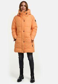 Padded coat in light orange with a hood, featuring a quilted design, zippered side pockets, and black hardware accents.
