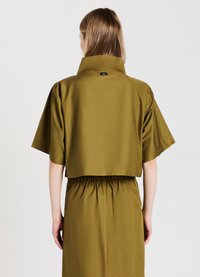 Camicia corta verde oliva con maniche corte e colletto alto, caratterizzata da una vita arricciata in un tessuto leggero e morbido.