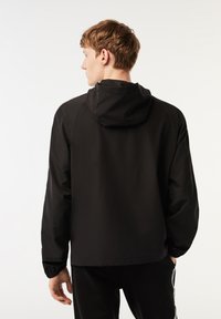 Svart huva-jacka med avslappnad passform, elastiska ärmar och en slät textur. Enkel design utan synliga stängningar eller mönster.