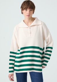 Gebreide pullover in crème met groene en witte horizontale strepen, voorzien van een geribde kraag, knoopsluiting en een relaxte pasvorm.
