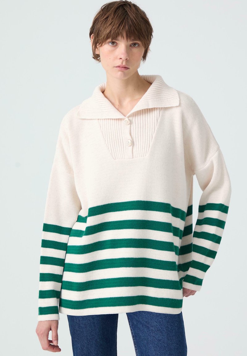 Gebreide pullover in crème met groene en witte horizontale strepen, voorzien van een geribde kraag, knoopsluiting en een relaxte pasvorm.