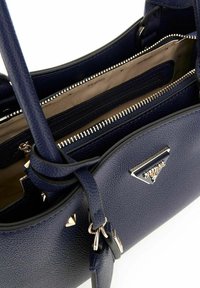 Sac à main en cuir grainé marine avec quincaillerie argentée, doté d'un compartiment zippé et d'une plaque logo triangulaire. L'intérieur comprend plusieurs poches.