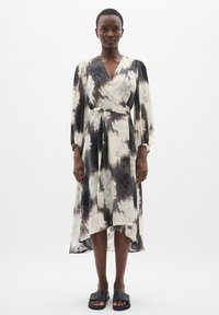 Rochie în pliuri alb-negru, cu un model floral, mâneci lungi și talie legată. Stilizată cu sandale plate negre.