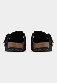 Ζεύγος μαύρων σανδαλιών χωρίς δέσιμο με πάτους από φελλό και ρυθμιζόμενα λουριά, θέα από πίσω σε απλό φωτεινό φόντο.