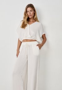 Top blanco recortado con mangas cortas y dobladillo elástico, combinado con pantalones blancos holgados que tienen una cintura con cordón y bolsillos laterales.