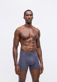 Vīriešu bokseršortiem tumši pelēkā krāsā, izgatavotiem no mīkstas kokvilnas maisījuma, ar zīmola jostu un pieguļošu dizainu ar plakanām šuvēm.