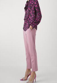 Musta paita, jossa on vaaleanpunaisia huulikuosisia, yhdistettynä vaaleanpunaisiin räätälöityihin housuihin ja kuumiin vaaleanpunaisiin nilkkaremmikenkiin. Silkkinen kangas, rento istuvuus.