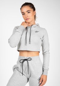 Grijze cropped hoodie met zwarte trekkoorden en logo, gecombineerd met bijpassende grijze trainingsbroek met een elastische tailleband en een zwarte strik.