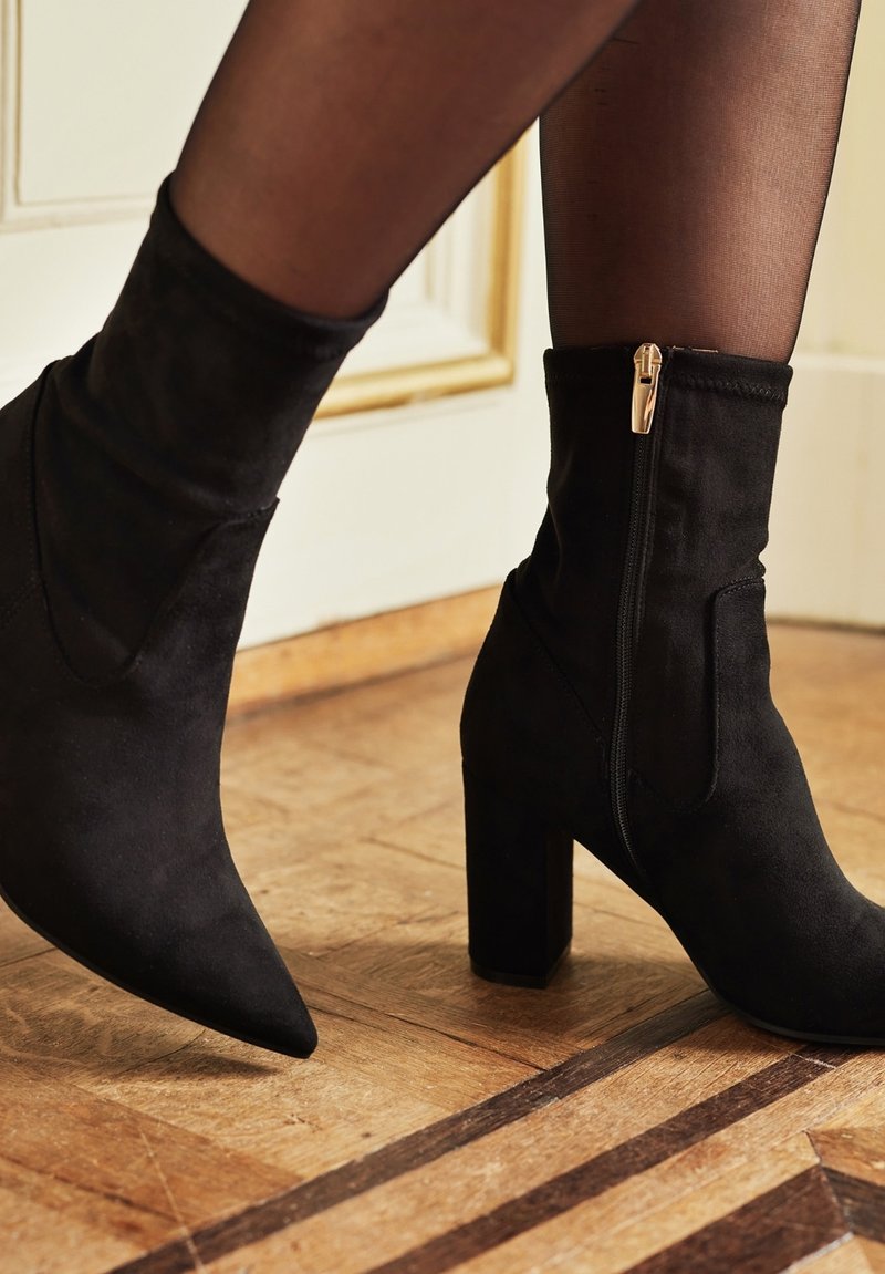 Schwarze Wildleder-Ankle Boots mit spitzem Zehenbereich und dicker Absätzen, ausgestattet mit einem seitlichen Reißverschluss und einer glatten Textur.