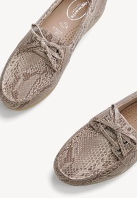 Paire de mocassins beige à motif peau de serpent avec nœuds et étiquette de largeur à l’intérieur, présentée sur fond blanc.