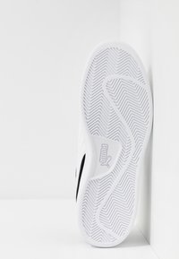 White sneaker with a smooth, synthetic upper and textured rubber sole featuring a zigzag pattern and a black logo accent on the side.