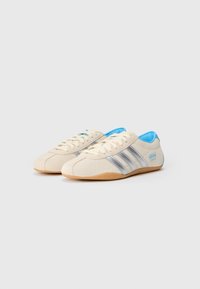 Lys beige semskede sneakers med sølvstriper, blå detaljer og gummisåle. Har snøring og rund tådesign.