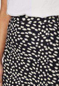 Černá sukně s květinovým vzorem bílých sedmikrásek se žlutými středy. Materiál se zdá být lehký s hladkou texturou.